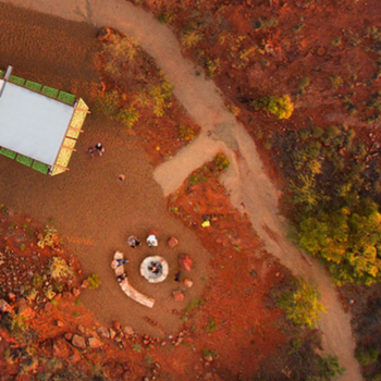 Aerial view of a red desert campsite with a fire pit and small group gathered nearby.